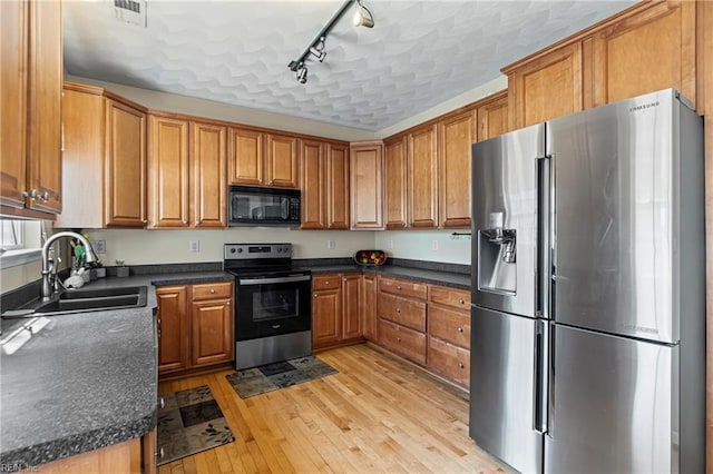 kitchen with brown cabinets, light wood-style flooring, a sink, dark countertops, and stainless steel appliances