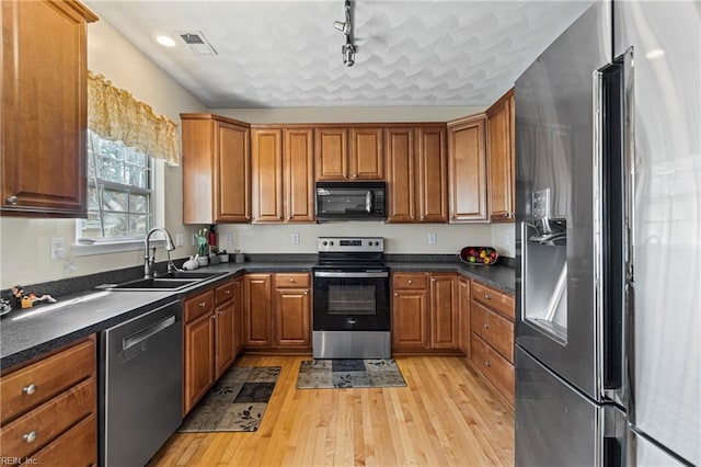 kitchen with dark countertops, visible vents, brown cabinets, stainless steel appliances, and a sink