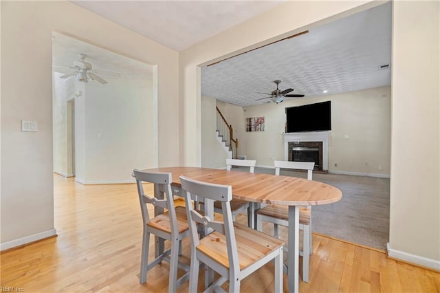 dining room featuring stairway, a ceiling fan, baseboards, a high end fireplace, and light wood-type flooring