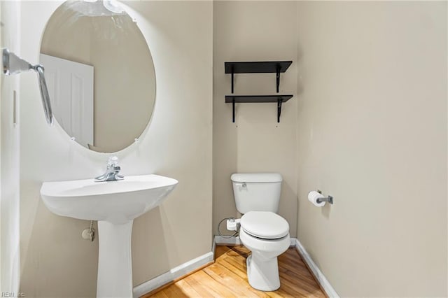 half bath with a sink, toilet, baseboards, and wood finished floors