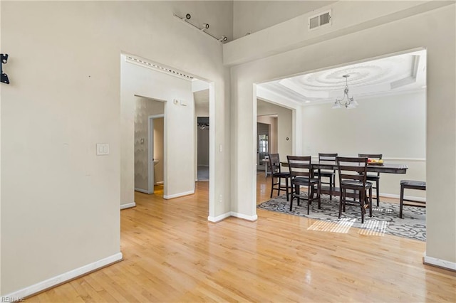 dining room featuring visible vents, baseboards, a chandelier, a tray ceiling, and light wood-style flooring