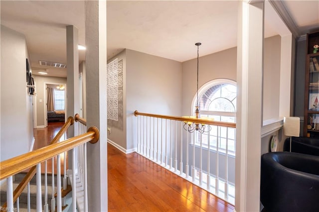 corridor featuring wood finished floors, baseboards, visible vents, an upstairs landing, and a chandelier