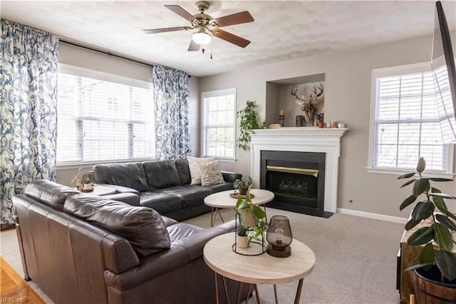 carpeted living room featuring plenty of natural light, ceiling fan, baseboards, and a fireplace with flush hearth