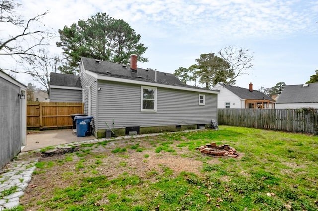 back of property with a fenced backyard, a chimney, a fire pit, a patio area, and a lawn