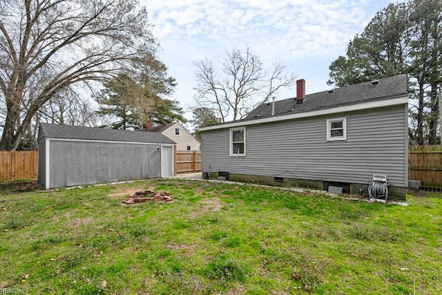 back of house with a fenced backyard, an outdoor fire pit, a yard, an outdoor structure, and a chimney