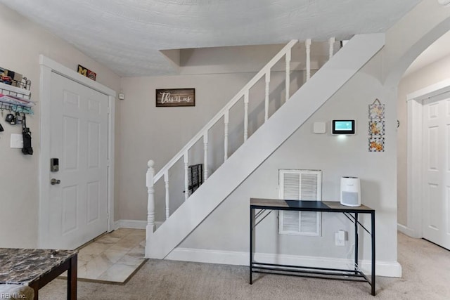 carpeted entrance foyer featuring arched walkways, stairs, and baseboards