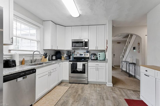 kitchen featuring a sink, stainless steel appliances, arched walkways, light wood-style floors, and white cabinets