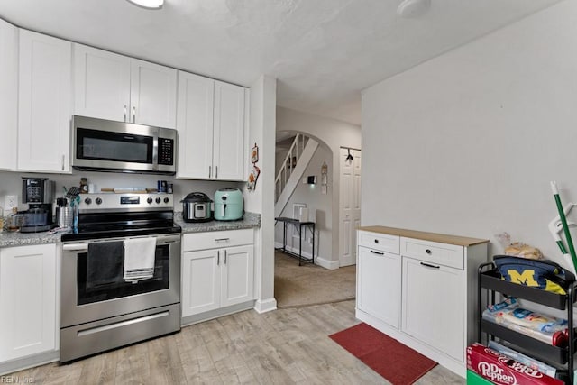 kitchen with white cabinetry, stainless steel appliances, arched walkways, light wood finished floors, and baseboards