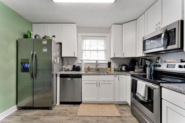 kitchen with light stone countertops, a sink, stainless steel appliances, light wood-style floors, and white cabinetry