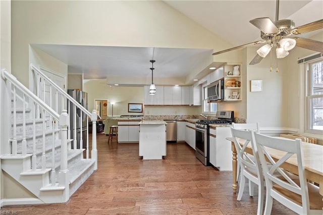 kitchen with pendant lighting, a kitchen island, wood finished floors, stainless steel appliances, and vaulted ceiling