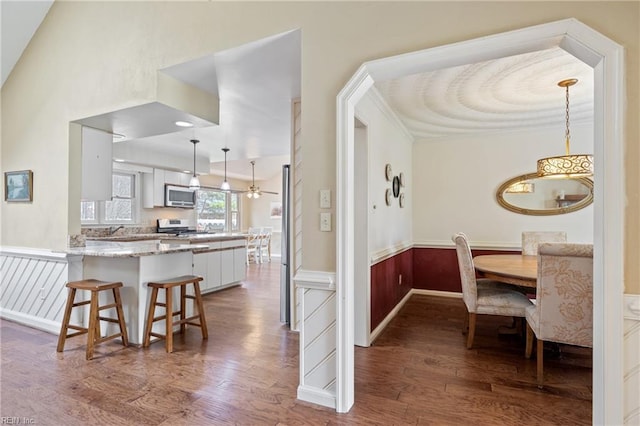 kitchen with a peninsula, appliances with stainless steel finishes, wood finished floors, and wainscoting