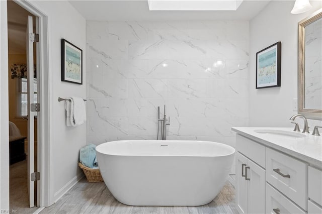 full bathroom featuring wood finished floors, tile walls, a skylight, a soaking tub, and vanity