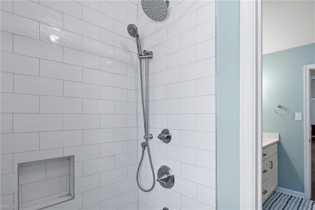 bathroom with tiled shower, vanity, and baseboards