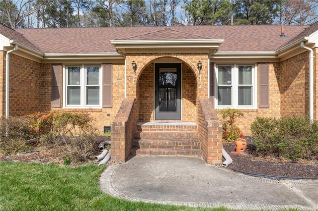 doorway to property featuring brick siding and roof with shingles