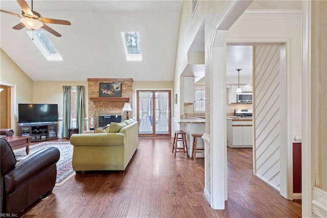 living room with vaulted ceiling with skylight, dark wood-type flooring, ceiling fan, and a fireplace