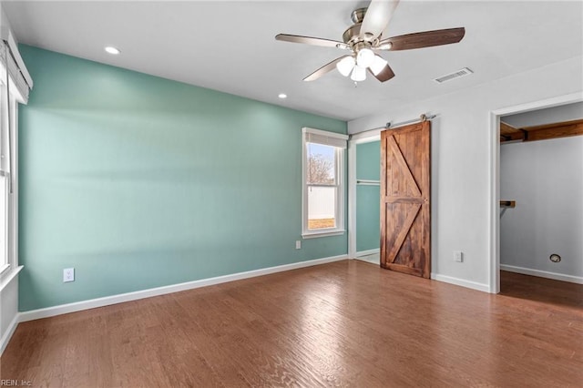 unfurnished bedroom featuring wood finished floors, visible vents, baseboards, a spacious closet, and a barn door