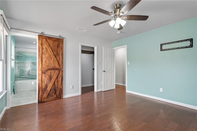 unfurnished bedroom with wood finished floors, visible vents, baseboards, a spacious closet, and a barn door