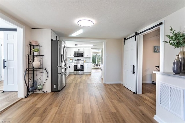 kitchen featuring stainless steel appliances, light wood-style floors, a textured ceiling, white cabinetry, and a barn door