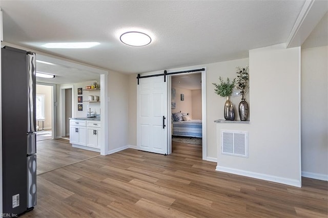 interior space with visible vents, baseboards, a barn door, wood finished floors, and a textured ceiling