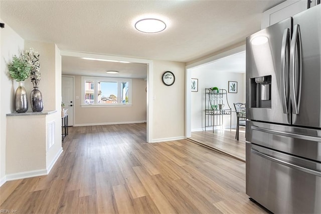 kitchen with baseboards, light wood-style flooring, white cabinets, a textured ceiling, and stainless steel fridge