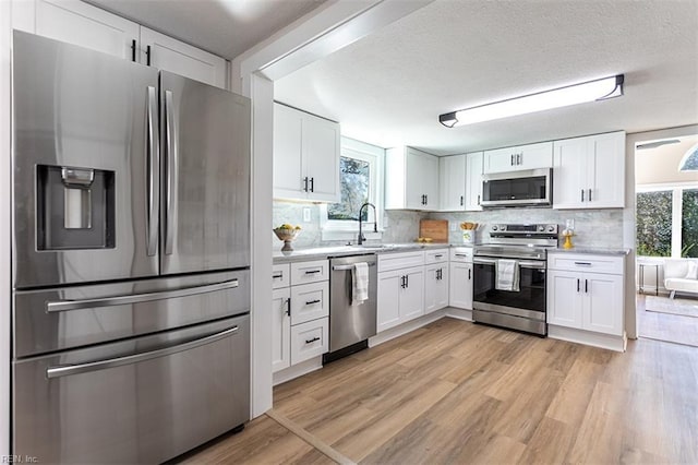 kitchen with a sink, light wood-type flooring, appliances with stainless steel finishes, and white cabinets