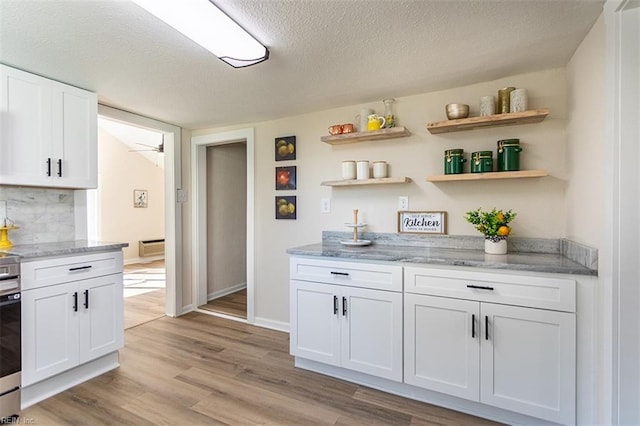 kitchen featuring white cabinetry, a textured ceiling, light wood-type flooring, and light stone countertops