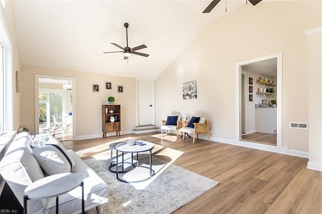 living area with visible vents, light wood-style flooring, high vaulted ceiling, and a ceiling fan