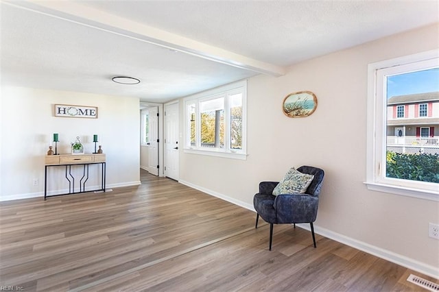 living area with wood finished floors, baseboards, visible vents, beam ceiling, and a textured ceiling