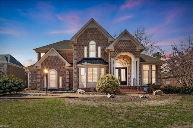 traditional home with a yard, brick siding, and roof with shingles