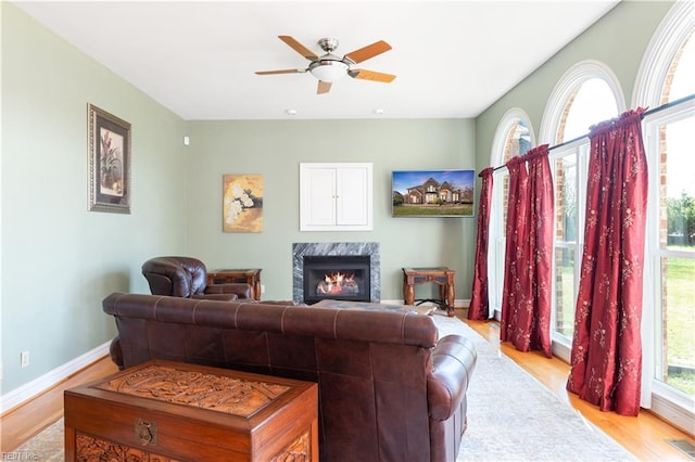 living area featuring a high end fireplace, light wood-style flooring, baseboards, and a wealth of natural light