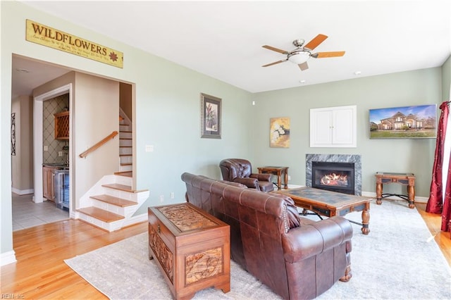 living area with a ceiling fan, light wood finished floors, a premium fireplace, baseboards, and stairs