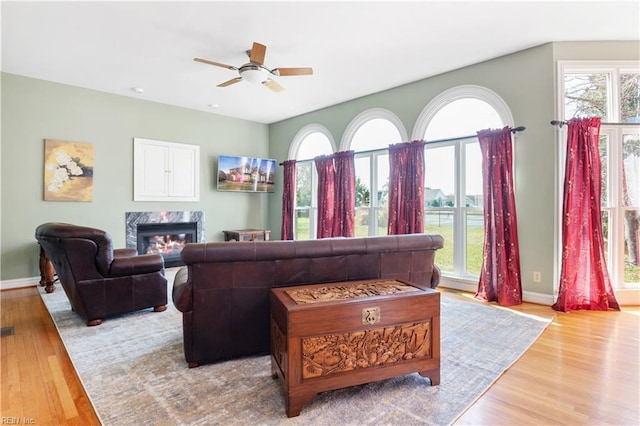 living area featuring baseboards, a ceiling fan, wood finished floors, and a fireplace