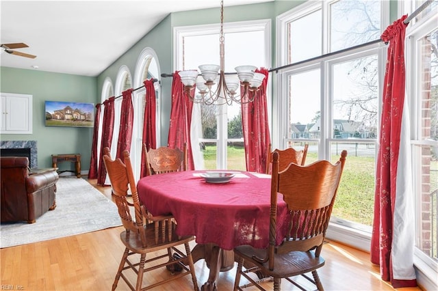 dining space featuring ceiling fan with notable chandelier, wood finished floors, and a high end fireplace