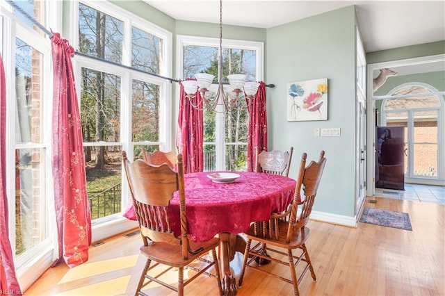 dining room featuring baseboards, a healthy amount of sunlight, an inviting chandelier, and light wood-style floors