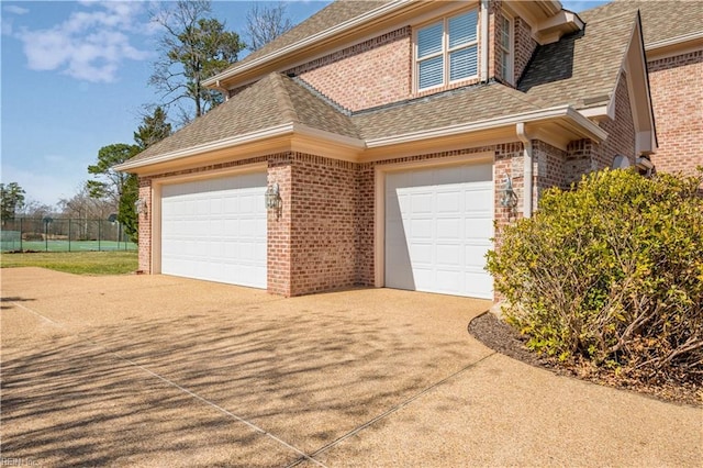 view of home's exterior with driveway, fence, brick siding, and roof with shingles