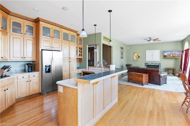 kitchen with glass insert cabinets, a center island with sink, pendant lighting, light wood-style flooring, and stainless steel fridge