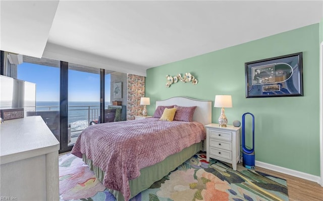 bedroom featuring baseboards, wood finished floors, a water view, and access to outside