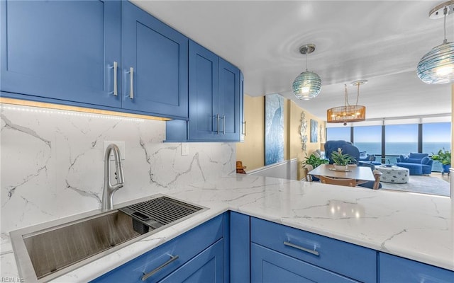 kitchen featuring tasteful backsplash, hanging light fixtures, blue cabinets, and a sink