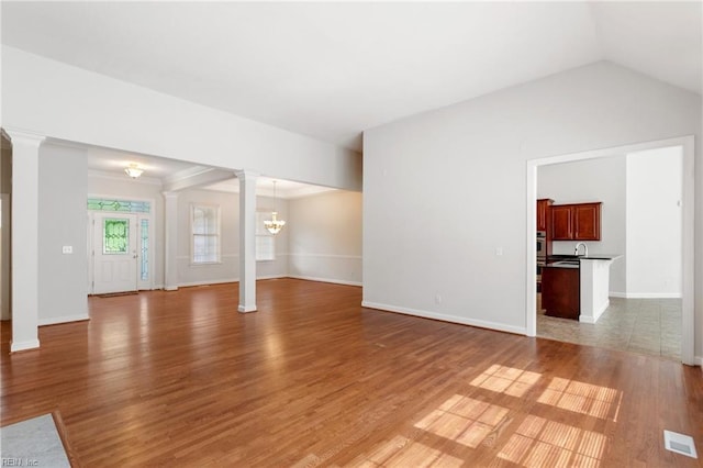 unfurnished living room with a notable chandelier, baseboards, light wood-style floors, decorative columns, and lofted ceiling