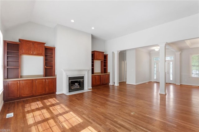 unfurnished living room featuring vaulted ceiling, light wood-style flooring, a fireplace with flush hearth, and ornate columns