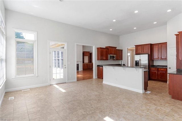 kitchen with a center island with sink, appliances with stainless steel finishes, dark countertops, a kitchen breakfast bar, and open floor plan