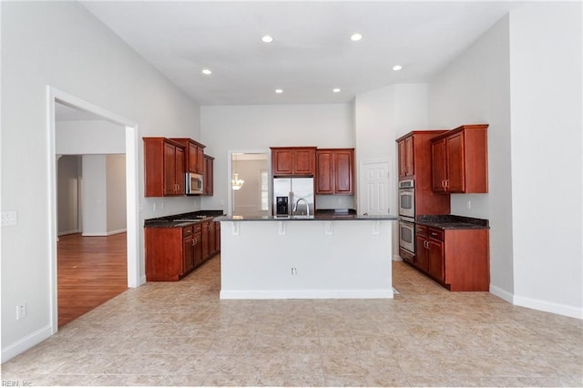 kitchen featuring dark countertops, baseboards, an island with sink, recessed lighting, and appliances with stainless steel finishes