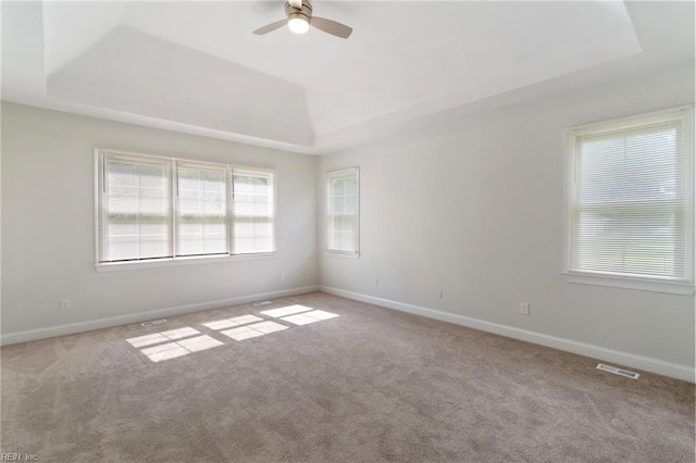 carpeted spare room featuring visible vents, a raised ceiling, and a ceiling fan