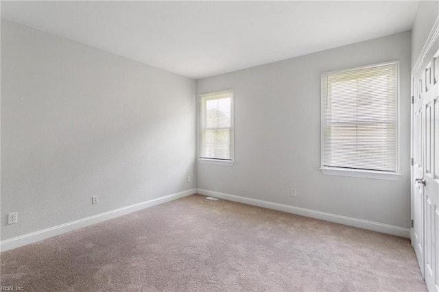 spare room featuring light colored carpet and baseboards