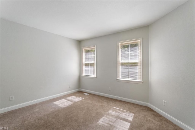 empty room featuring baseboards, light carpet, and visible vents