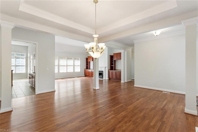 unfurnished living room with an inviting chandelier, ornamental molding, a tray ceiling, and wood finished floors