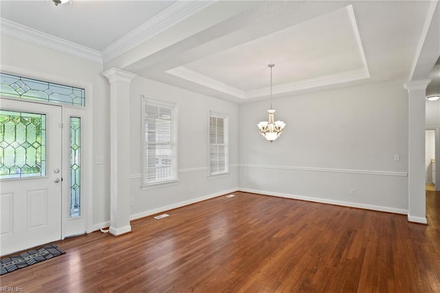 entryway with a tray ceiling, an inviting chandelier, wood finished floors, and ornate columns