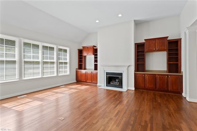 unfurnished living room with baseboards, a fireplace with flush hearth, lofted ceiling, and wood finished floors