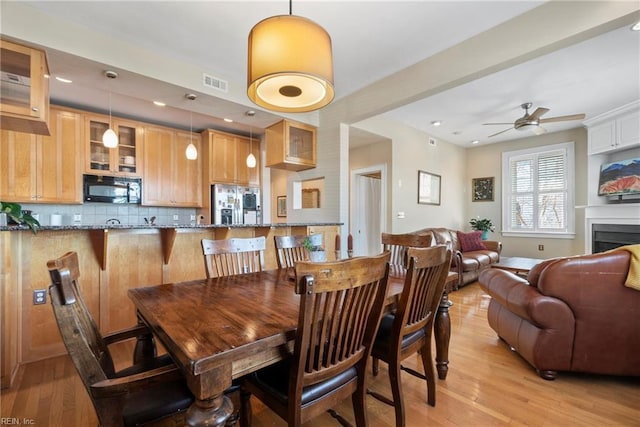 dining area with a ceiling fan, light wood-style flooring, a fireplace, and visible vents