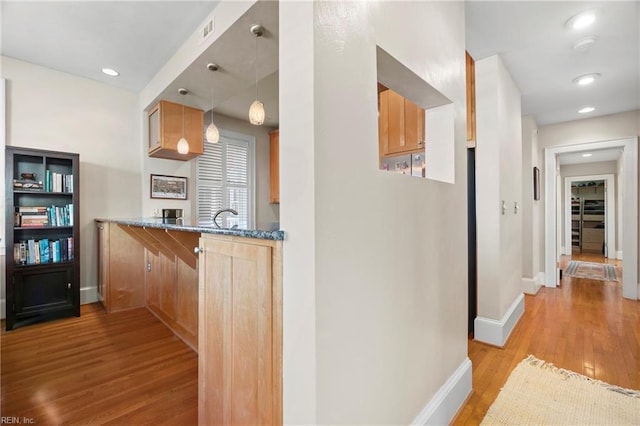 kitchen with baseboards, stone counters, light wood-style flooring, a sink, and pendant lighting